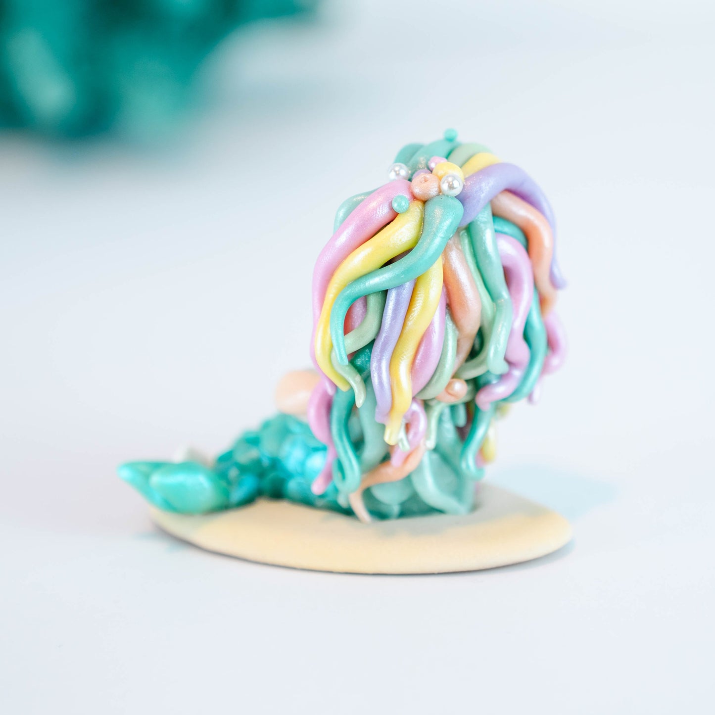 Mermaid figurine with colorful hair and tail on a light sand colored base
